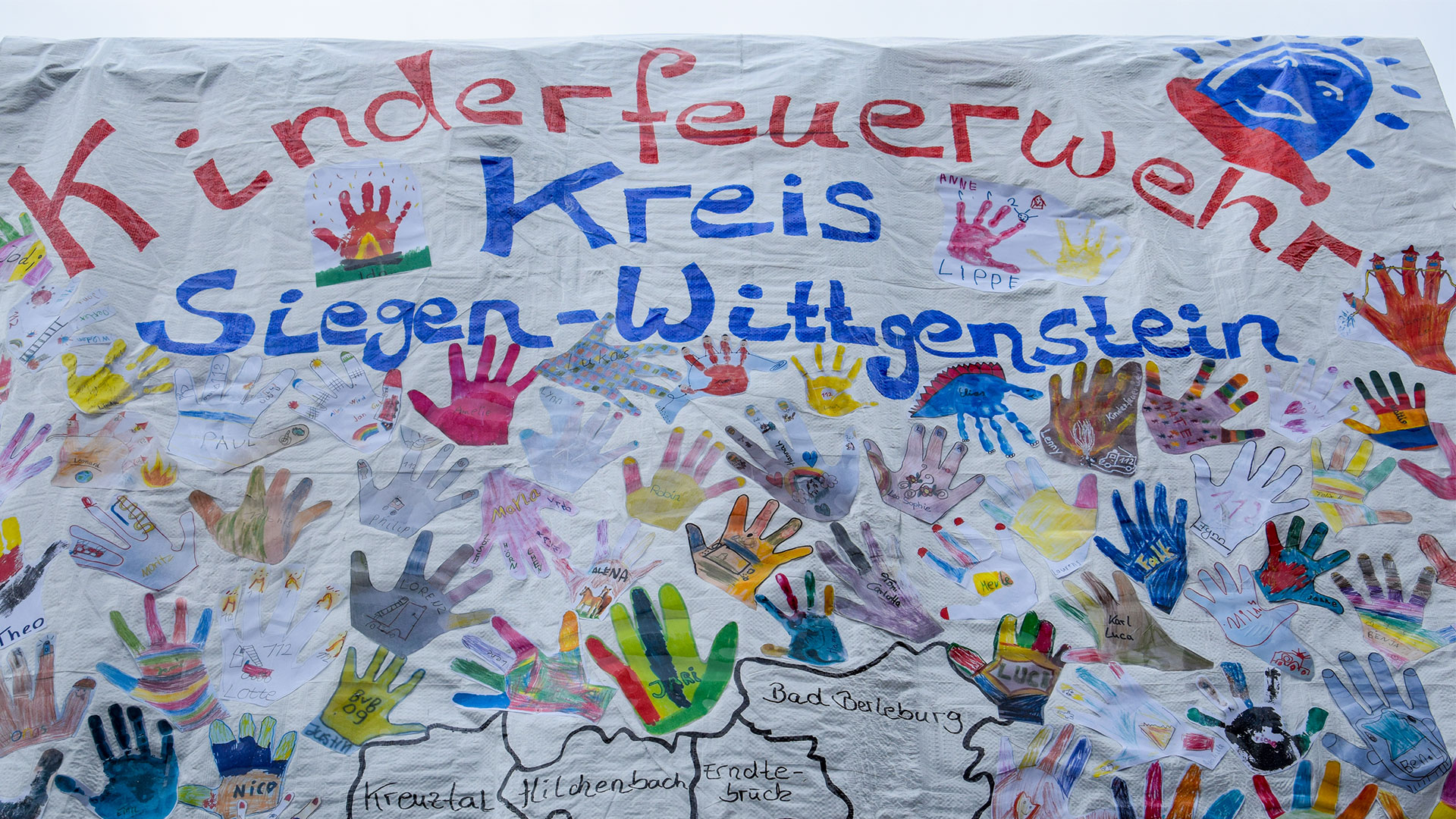 Farbige Kinderhandabdrücke auf einer großen Leinwand, auf dieser steht Kinderfeuerwehr, Kreis Siegen-Wittgenstein